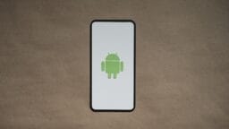 A smartphone displays the green Android robot logo on a white screen, placed on a plain brown surface.