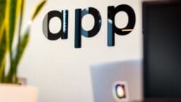 Black letters spelling app are mounted on a white wall near a plant and a blurred laptop in the foreground.