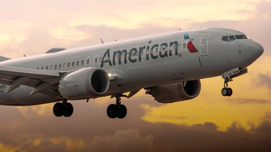 An American Airlines jet aircraft is landing or taking off against a cloudy sunset sky.