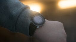 A person wearing a dark green digital watch looks at their wrist against a blurred background with bright lights.