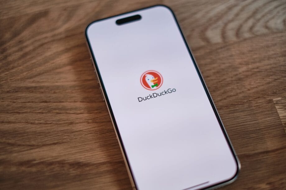 A smartphone on a wooden table displays the DuckDuckGo search engine logo and name on its screen.