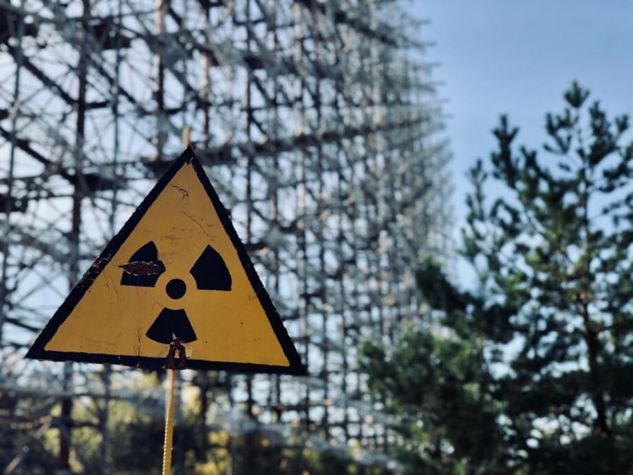 A yellow radiation warning sign stands in front of a large metal structure and trees under a clear sky.
