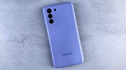 A purple Samsung smartphone with three rear camera lenses is placed on a light gray surface.