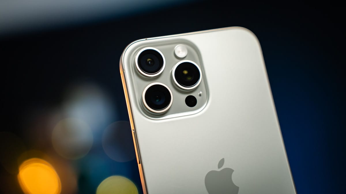 Close-up of the rear camera system on a silver iPhone, showing three lenses and the Apple logo.