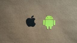 Black Apple logo and green Android robot logo on a plain brown background, centered side by side.