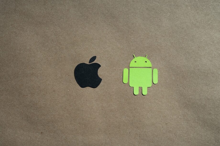 Black Apple logo and green Android robot logo on a plain brown background, centered side by side.
