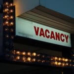 A lit sign with the word “VACANCY” in red letters, surrounded by small lightbulbs, indicating available rooms.