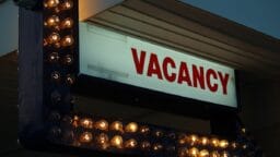 A lit sign with the word “VACANCY” in red letters, surrounded by small lightbulbs, indicating available rooms.