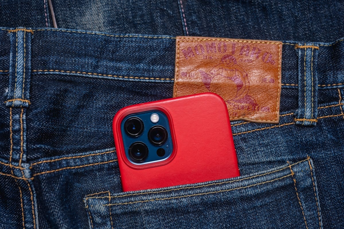 A smartphone with a red case is partially visible in the back pocket of blue denim jeans.
