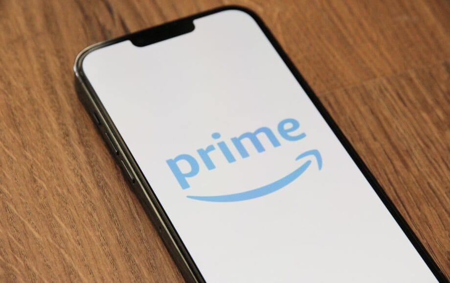 A smartphone displaying the Amazon Prime logo on its screen, placed on a wooden surface.