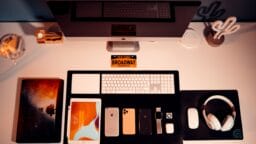 Neatly organized desk with an iMac, keyboard, iPad, various smartphones, AirPods, headphones, mouse, and a Broadway souvenir.