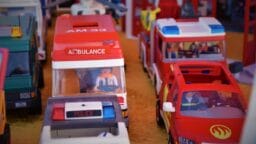 Close-up of toy emergency vehicles, including an ambulance, police car, and fire car, with plastic figures inside on a play surface.