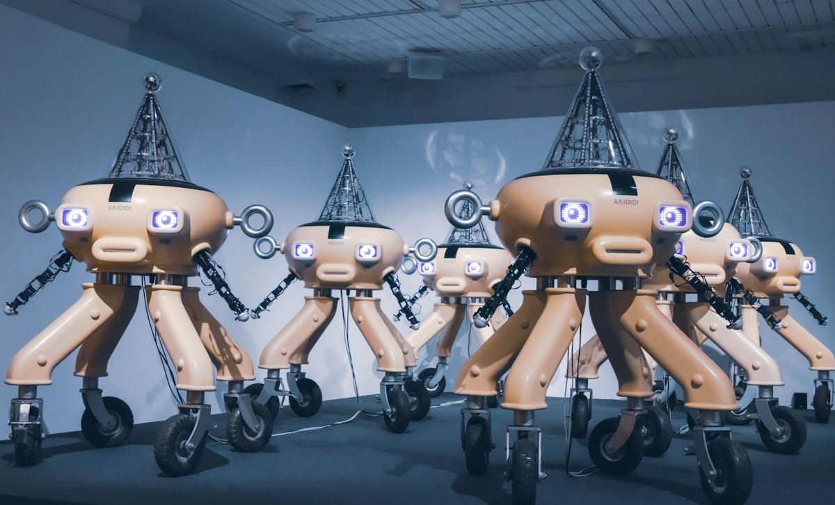 A group of humanoid robots with wheeled legs and cone-shaped heads stand together in a room with a white ceiling.