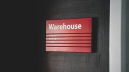 A red sign on a dark wall reads Warehouse with categories for Shipping, Receiving, and Service listed below.