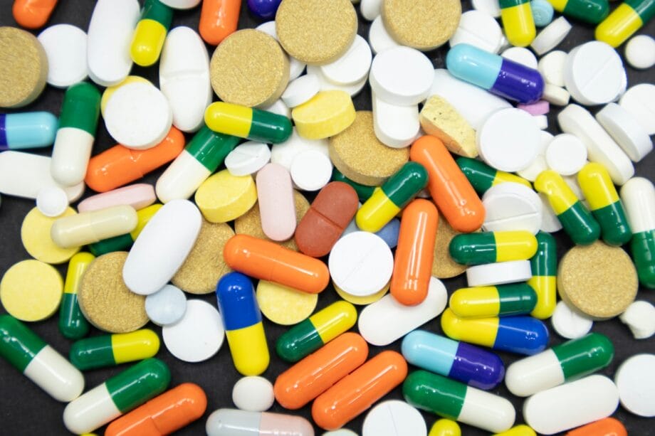 A variety of colorful pills, capsules, and tablets scattered on a dark surface.