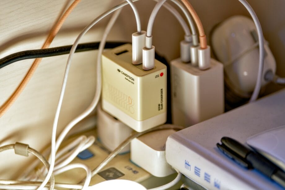 Several electronic devices and cables plugged into a multi-outlet power strip and USB charger on a cluttered surface.