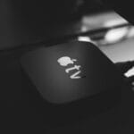 A close-up of an Apple TV streaming device with connected cables, placed on a reflective surface.