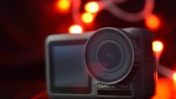A close-up of an Osmo Action camera with red and white blurred lights in the background.