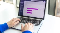 Person using a MacBook Pro with a data analytics dashboard displaying bar graphs on the screen.