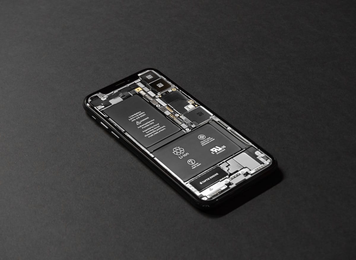 A smartphone with its back cover removed, revealing internal components like the battery and circuitry, placed on a dark surface.