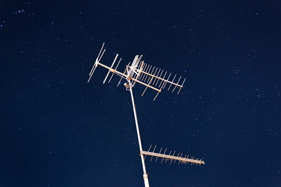 A TV antenna on a tall pole is set against a clear night sky filled with stars.