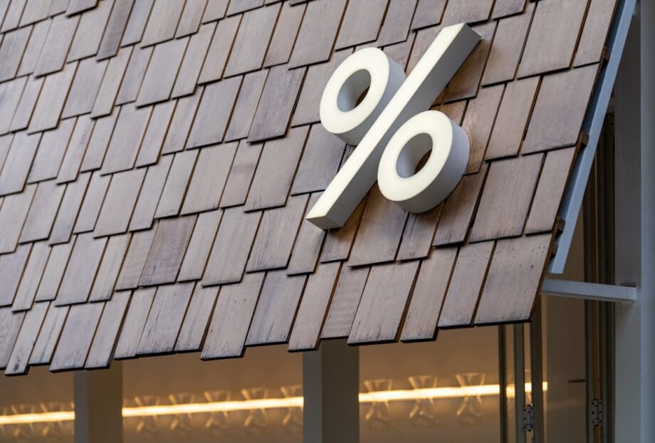 A large illuminated percent sign is mounted on a wooden shingle roof above a building entrance.