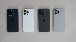 Four iPhones in different colors—blue, white, black, and silver—are arranged side by side on a light surface, showing their backs.