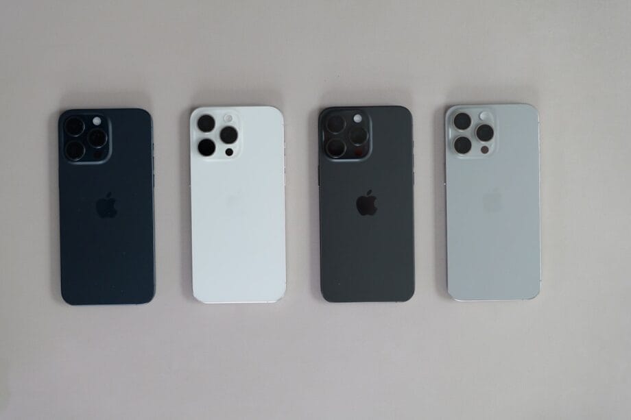 Four iPhones in different colors—blue, white, black, and silver—are arranged side by side on a light surface, showing their backs.