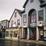 A row of colorful small shops and a breakfast restaurant on a quiet, wet street in a quaint town.