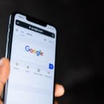 A hand holding a smartphone displaying the Google search homepage on its screen.
