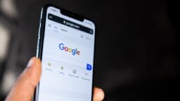 A hand holding a smartphone displaying the Google search homepage on its screen.