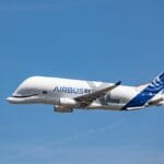 An Airbus Beluga cargo aircraft in flight against a clear blue sky.