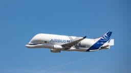 An Airbus Beluga cargo aircraft in flight against a clear blue sky.