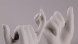 Two white sculpted hands making a pinky promise gesture against a plain light background.