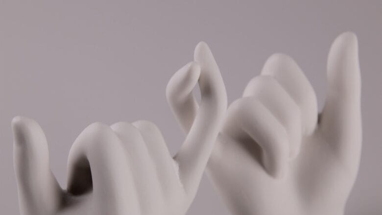 Two white sculpted hands making a pinky promise gesture against a plain light background.