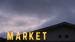 Large yellow MARKET sign is illuminated in front of a building at dusk, with a cloudy sky in the background.