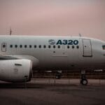 Side view of an Airbus A320 airplane parked on the tarmac with overcast skies in the background.