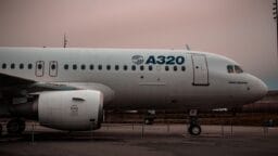 Side view of an Airbus A320 airplane parked on the tarmac with overcast skies in the background.