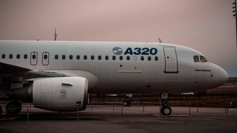 Side view of an Airbus A320 airplane parked on the tarmac with overcast skies in the background.