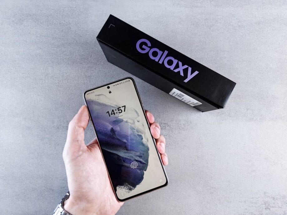 A person holds a Samsung Galaxy smartphone with its box placed on a light gray surface.