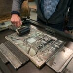 A person rolls ink onto a printing plate on a letterpress machine in a workshop setting.