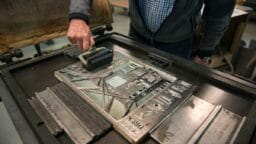 A person rolls ink onto a printing plate on a letterpress machine in a workshop setting.