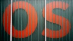 Large red letters O and S are partially visible behind a paneled glass wall with vertical metal bars.