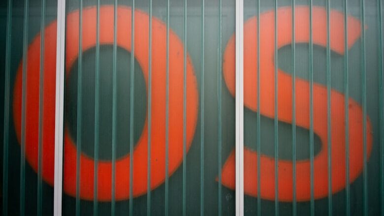 Large red letters O and S are partially visible behind a paneled glass wall with vertical metal bars.