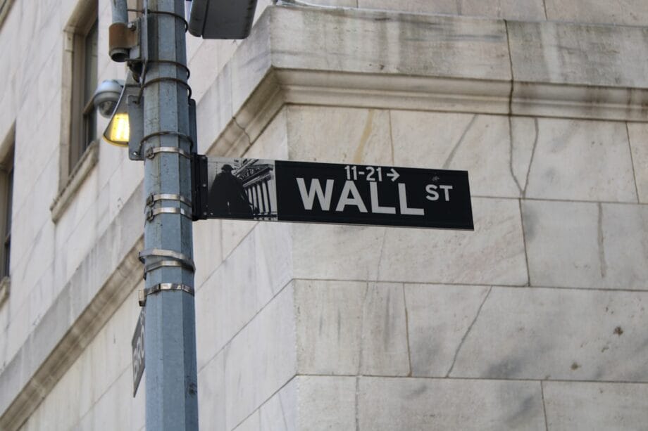 A Wall Street street sign attached to a metal pole in front of a stone building.