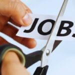 A hand uses scissors to cut a piece of paper with the word JOBS printed on it.