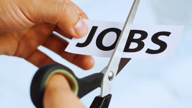 A hand uses scissors to cut a piece of paper with the word JOBS printed on it.