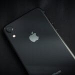 A black iPhone lying face down on a dark surface, showing the Apple logo and rear camera.