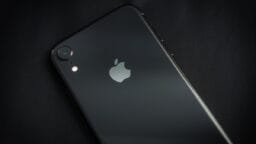 A black iPhone lying face down on a dark surface, showing the Apple logo and rear camera.