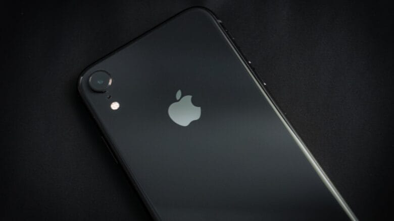 A black iPhone lying face down on a dark surface, showing the Apple logo and rear camera.